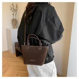 Detail of dark brown suede bucket bag with dual ring handles and leather strap