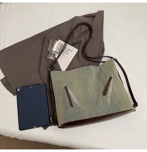 Detail of blue denim tote bag with brown leather bottom and sleek metal zippers