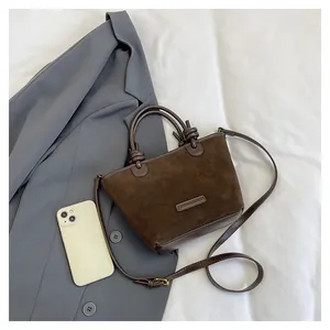 Detail of coffee suede bucket bag with knot handle and strap on a blazer background