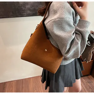 Detailed view of brown suede shoulder bag with gold button on a pleated skirt outfit