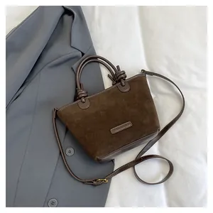 Close-up of brown suede bucket bag featuring leather trim and knotted handle detail
