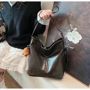 Détail de la texture cuir mat souple d'un grand cabas marron avec charm d'ours