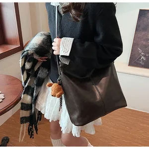 Détail d'un grand sac cabas en cuir marron avec coutures verticales et breloque ourson