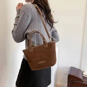 Retro brown suede bucket bag with cylindrical knotted handles and adjustable crossbody strap