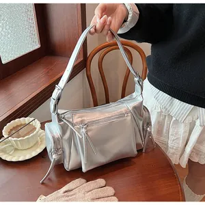 Détail d'un sac à bandoulière argenté métallisé avec plusieurs fermetures éclair sur table