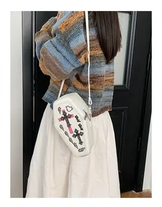 White coffin-shaped crossbody bag with gothic cross embroidery shown on a model