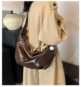 Detalle de un bolso hobo marrón brillante con costuras de contraste y colgante de béisbol