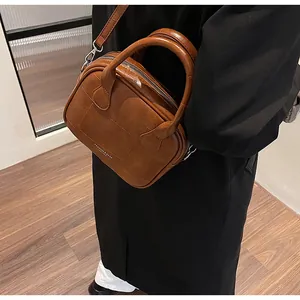Brown vintage pillow handbag with textured pattern worn as a crossbody bag by a model