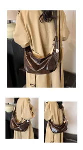 Detalle de un bolso hobo marrón brillante con colgante de béisbol y correa ancha