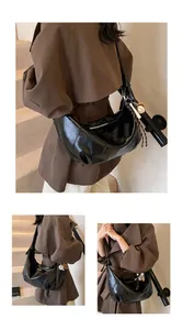 Detalle del bolso hobo de cuero brillante negro con colgante de béisbol y cremallera