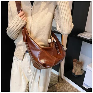 Detalle de bolso hobo marrón con costuras blancas y accesorio de béisbol decorativo