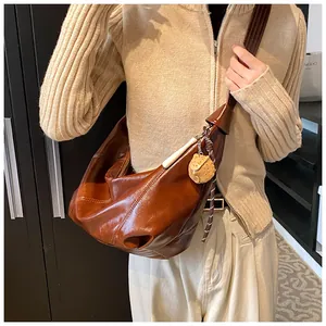 Detalle del bolso media luna retro de cuero marrón con colgante de oso y correa ancha
