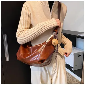 Detalle de bolso retro de cuero marrón con costuras blancas y colgante de oso
