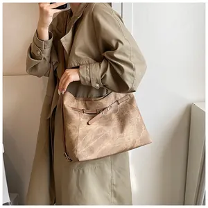 Brown vintage tote bag with cracked leather texture shown on person wearing khaki trench coat