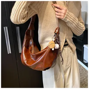 Detalle de bolso hobo marrón oscuro brillante con cremallera y colgantes de béisbol