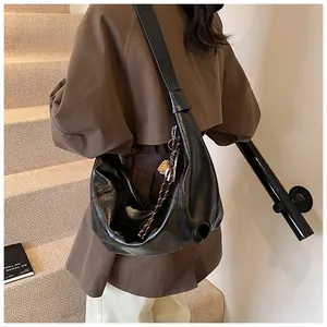 Detalle del bolso de media luna negro con textura de cuero brillante y correa anudada