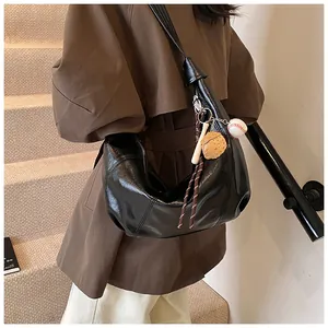 Detalle de bolso hobo grande de cuero negro aceitado con dijes deportivos y correa ancha