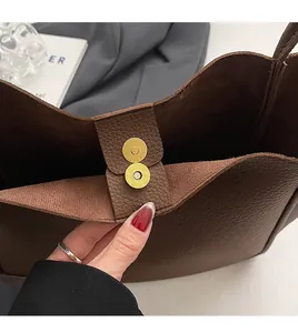 Detail of golden magnetic clasp on dark brown lychee textured leather tote bag