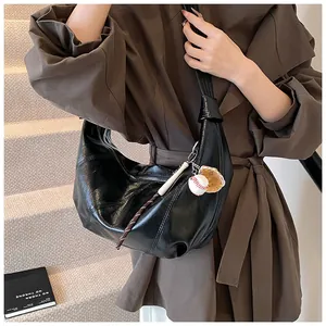 Detalle del bolso de media luna negro en cuero brillante con colgantes de béisbol en modelo