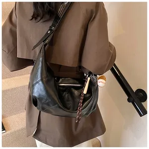 Detalle del bolso hobo minimalista en cuero sintético negro con dije de béisbol único