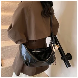Detalle de un bolso bandolera negro de media luna con un pequeño colgante de béisbol
