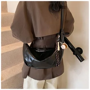 Detalle del bolso hobo negro de media luna con colgante de béisbol en abrigo marrón