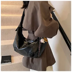Detalle de un bolso hobo grande negro en cuero brillante con colgantes de béisbol y correa