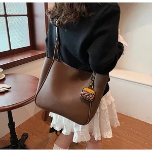 Detailed side view of a large brown leather tote bag with stylish leopard print charm