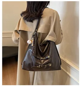 Detail of vintage dark brown tote bag with metal buckles and baseball charm on a trench coat