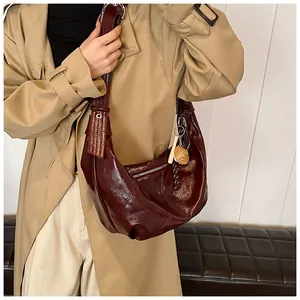 Detalle de bolso medialuna granate oscuro con piel brillante y dije de perro