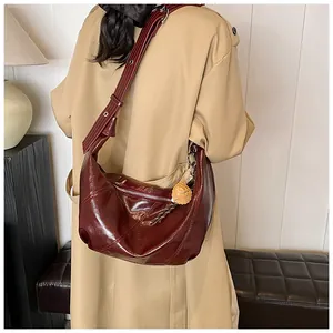 Detalle de bolso hobo burdeos brillante con correa ajustable y colgante decorativo