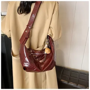 Detalle de bolso hobo de cuero burdeos con correa ajustable sobre gabardina beige