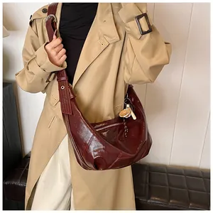 Detalle de bolso hobo granate brillante con correa ancha y colgante floral de moda