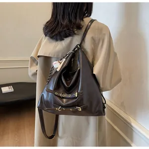 Detail of dark brown glossy leather tote bag with buckle straps and a baseball charm