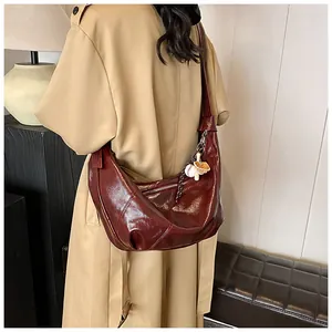 Detalle del bolso de media luna en charol burdeos con un elegante colgante de flores