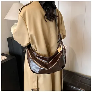 Detalle de bolso de cuero brillante marrón oscuro combinado con una gabardina caqui