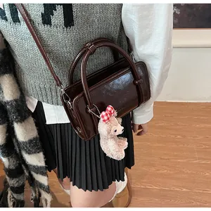 Detail of dark brown glossy handbag featuring a pink teddy bear charm and dual handles