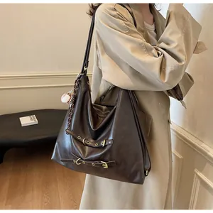 Detail of dark brown leather tote bag with gold metal buckles and a baseball charm