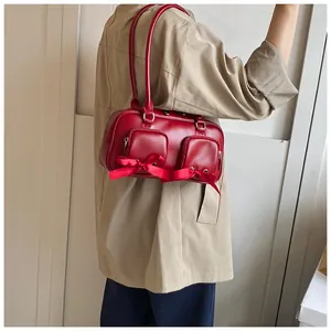 Detail of red PU shoulder bag featuring bow decor, silver zippers, and twin pockets