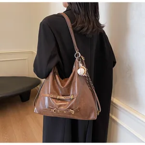 Detail of vintage brown leather tote bag featuring decorative straps and baseball charm