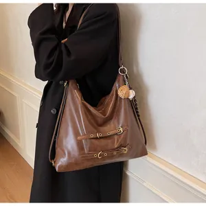 Close-up of vintage brown leather tote with metallic buckles and baseball charm