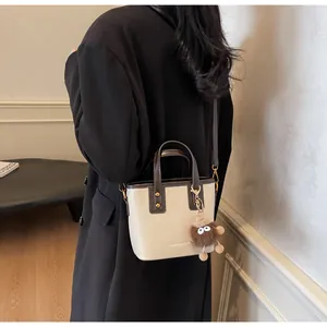 Détail du sac seau bicolore crème et marron avec rivets et breloque pelucheuse