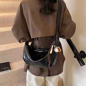 Elegante bolso hobo negro con colgantes de béisbol y cuero brillante puesto en modelo