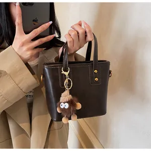 Détail du sac seau en cuir PU marron foncé avec charm monstre en peluche et rivets dorés