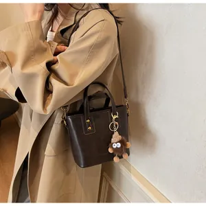Détail du sac à main marron foncé avec ferrures dorées et breloque monstre en peluche