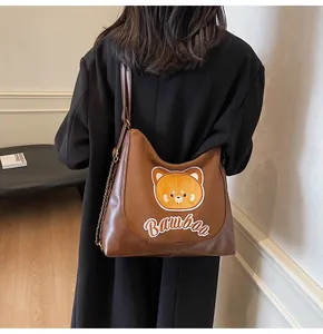 Détail d'un sac à bandoulière en cuir marron avec patch ours et sangle en chaîne