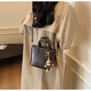 Mannequin portant un mini sac seau marron foncé avec charm peluche et bandoulière