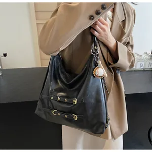 Detail of a large black leather tote bag with retro buckle straps and a sports charm
