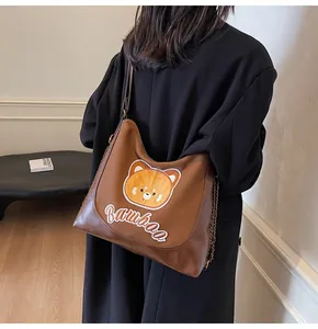Détail de broderie d'ours et chaîne métallique sur sac bandoulière en cuir marron