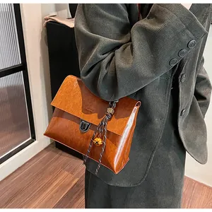 Detail der braunen Vintage-Ledertasche mit Metallschloss und geflochtenem Anhänger